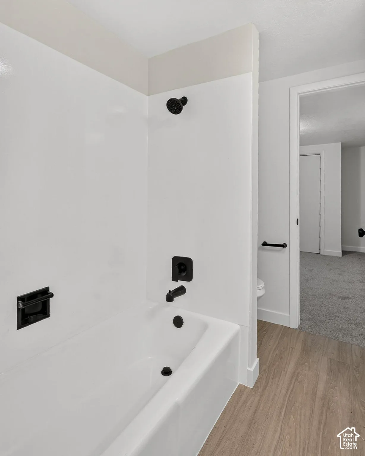 Bathroom featuring a white acrylic tub surround, matte black shower fixtures, matching black hardware, and wood-finish flooring