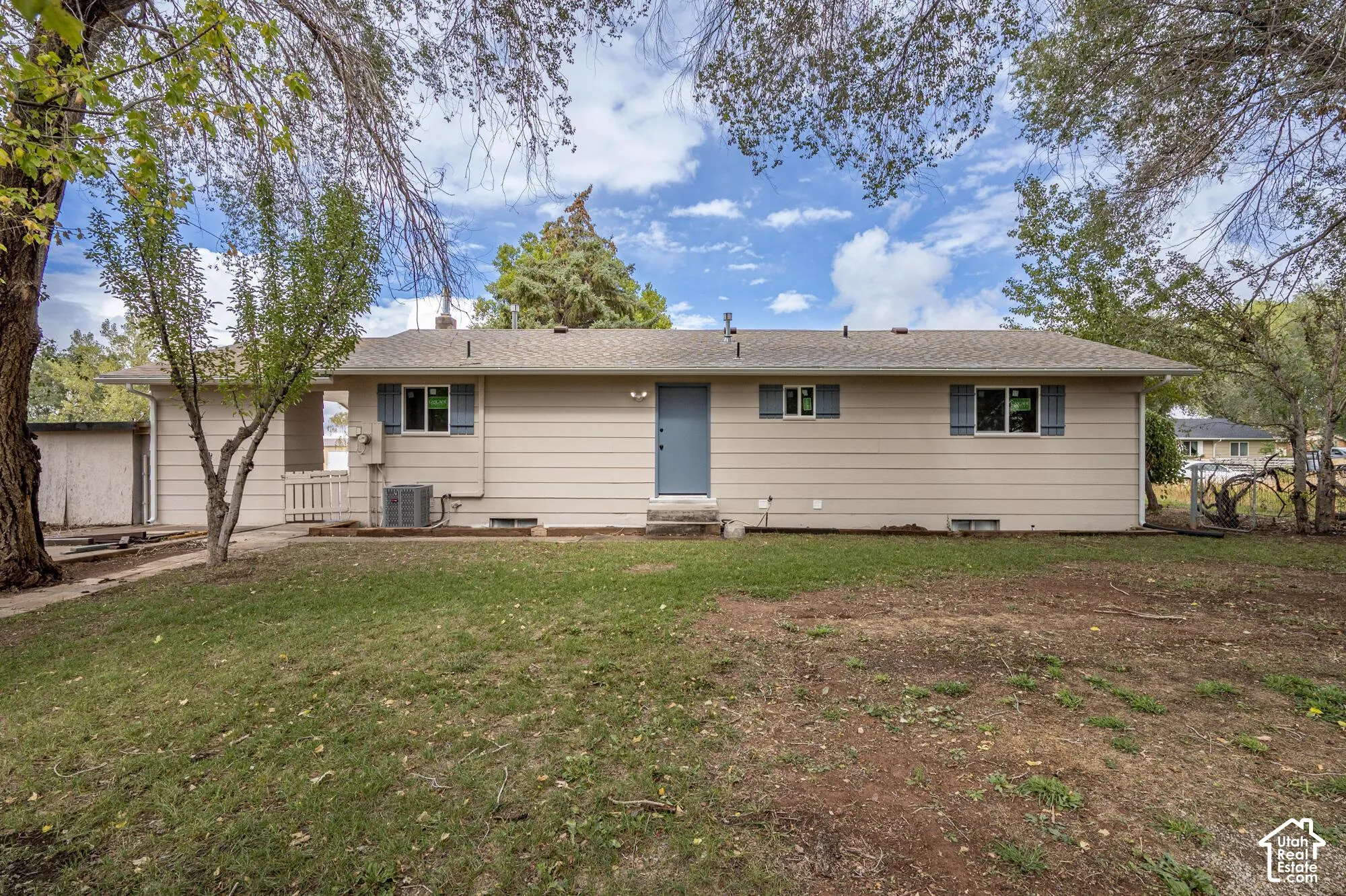 Single-story exterior featuring light-colored horizontal siding, a central solid-core entry door, functional window shutters, and a covered side carport area