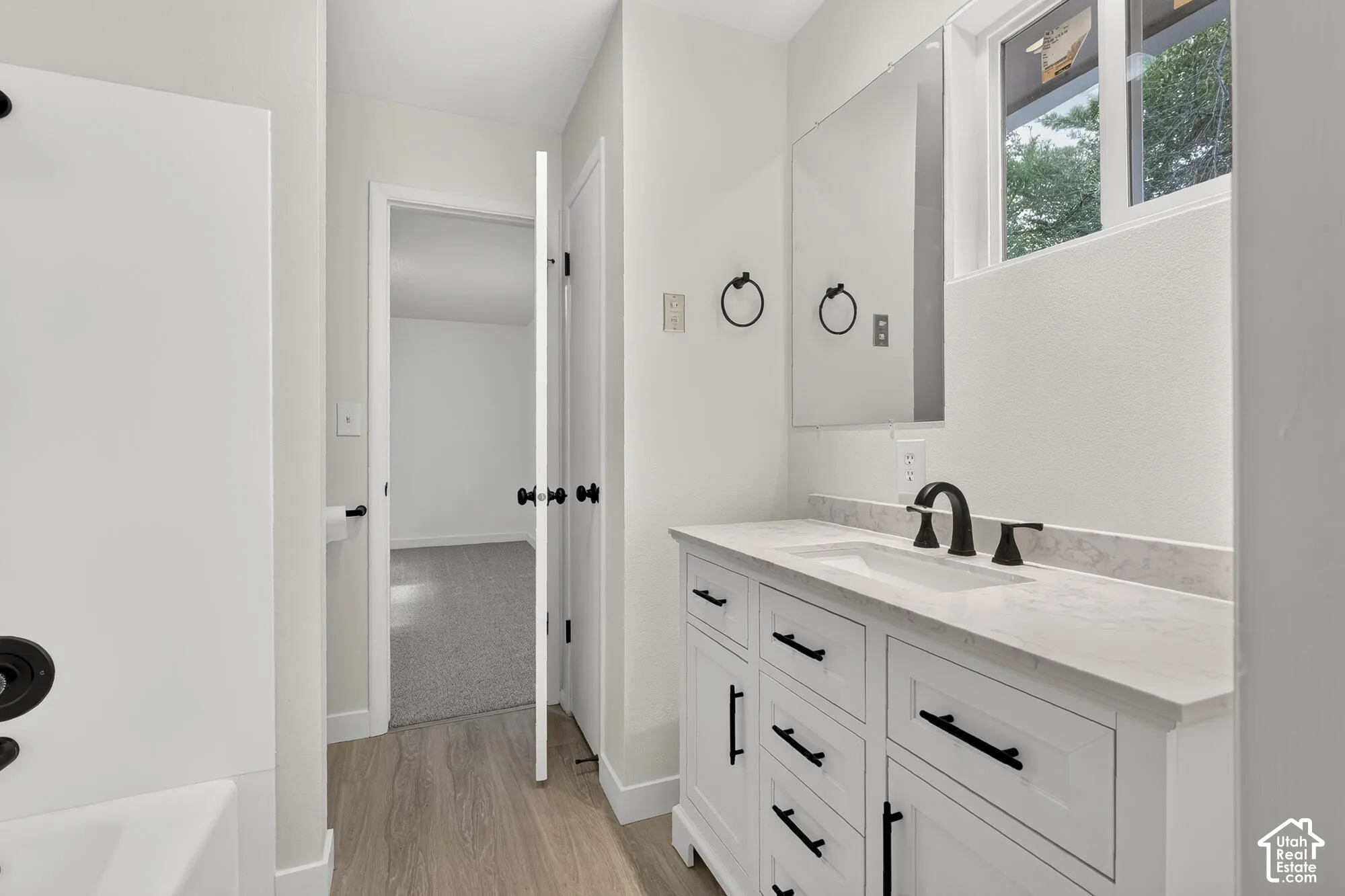 Bathroom featuring a white shaker-style vanity with stone-composite countertop, matte black widespread faucet, integrated rectangular sink, and large wall-mounted mirror