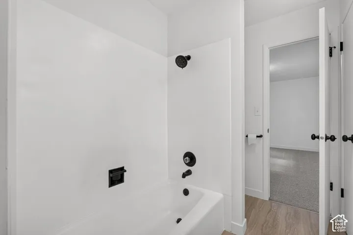 Bathroom featuring a white composite tub surround, matte black shower head, matching black faucet hardware, and wood-finish flooring