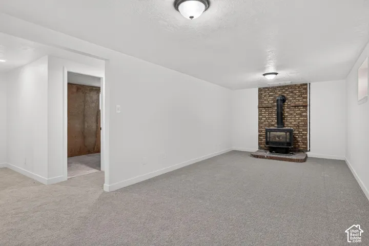 Interior space featuring neutral carpeting, a brick hearth, and a wood-burning stove with a metal chimney pipe