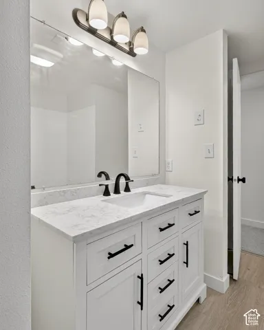 White vanity with a stone-composite countertop, undermount sink, matte black hardware, and a three-light fixture over a wall-to-wall mirror