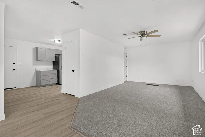 Interior space featuring wood-finish flooring, grey cabinetry with stone-finish countertops, neutral wall-to-wall carpeting, and a ceiling-mounted fan