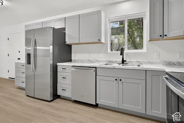 Kitchen featuring light gray shaker-style cabinetry, stainless steel appliances, stone-patterned countertops, a dual-basin sink with a matte black faucet, and wood-finish flooring