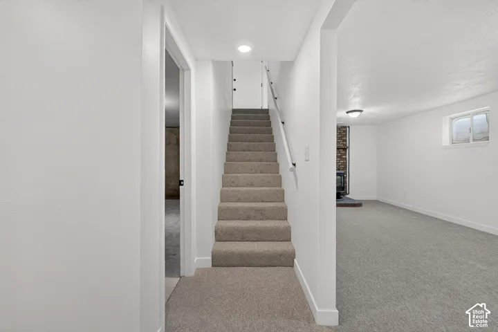 Carpeted stairway with a minimalist handrail, neutral wall-to-wall carpeting, recessed lighting, and a brick fireplace surround