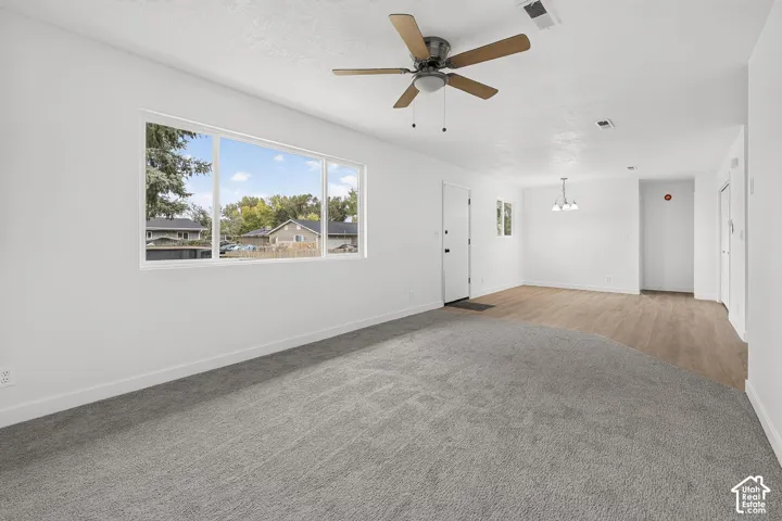 Neutral interior space featuring wood-finish flooring, wall-to-wall carpeting, a large picture window, and a ceiling fan with integrated lighting