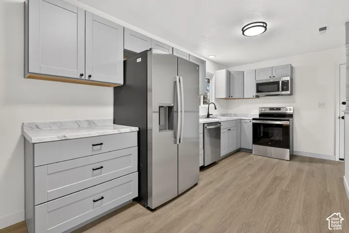 Kitchen featuring gray shaker-style cabinetry, patterned stone-finish countertops, stainless steel appliances, and wood-finish flooring