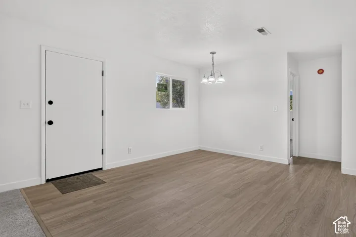 Interior space featuring wood-finish flooring, white walls, a dual-pane window, and a multi-arm pendant light fixture