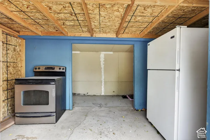 Utility area featuring an exposed wood-beam ceiling, concrete flooring, stainless steel electric range, and refrigerator