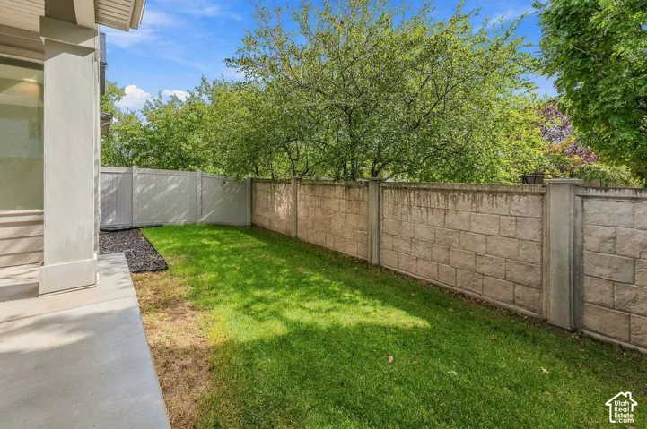 Rear exterior space featuring a concrete patio, grassy lawn, stone-textured masonry perimeter wall, and a vinyl privacy fence