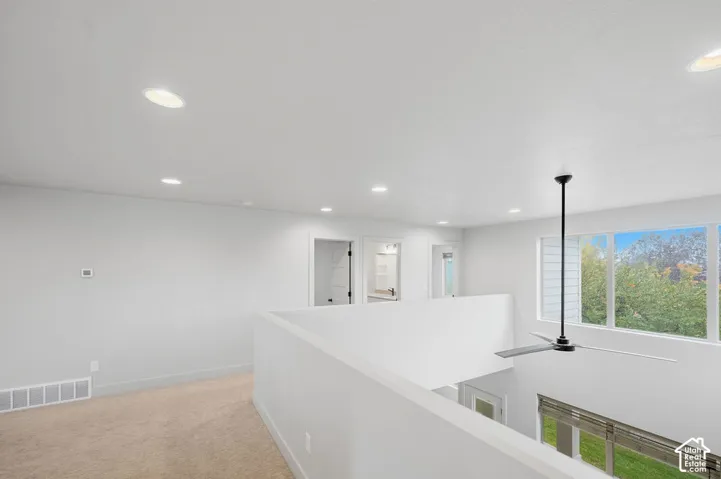 Open loft area featuring neutral carpeting, recessed ceiling lighting, a modern ceiling fan, and large windows