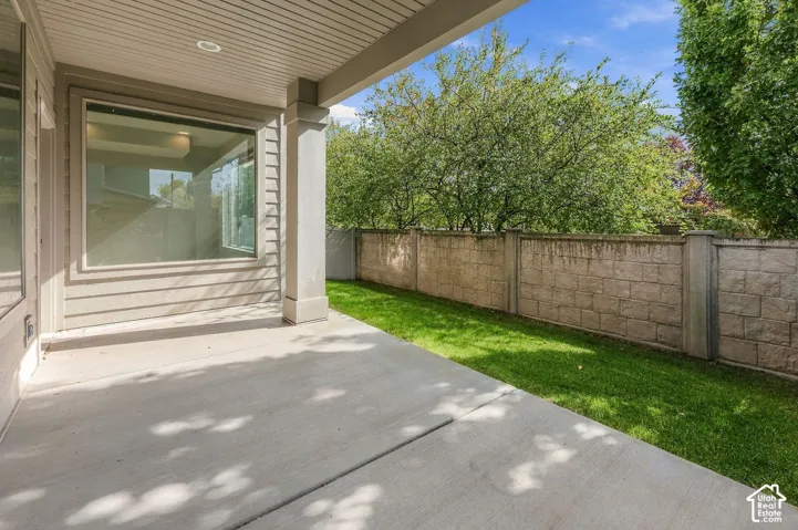 Covered concrete patio featuring a square column, recessed lighting, expansive lawn, and concrete masonry unit perimeter wall