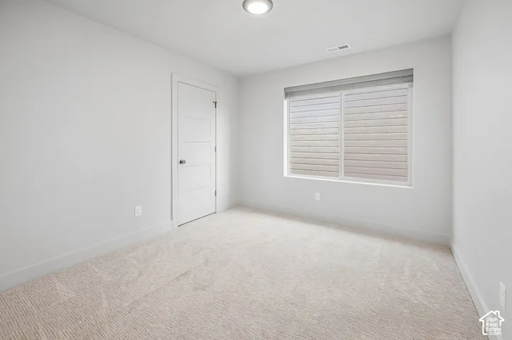Neutral-toned interior space featuring wall-to-wall carpeting, a multi-panel interior door, a horizontal sliding window with fitted blinds, and a flush-mount ceiling light fixture