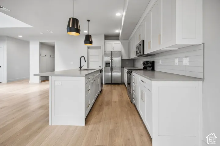 Kitchen featuring white cabinetry, solid-surface countertops, horizontal tile backsplash, wood-finish flooring, and matte black pendant lighting