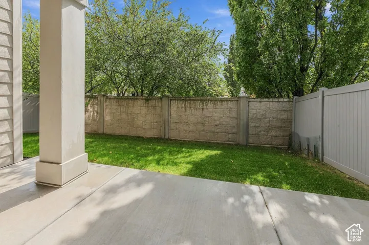 Concrete patio featuring a support column, manicured lawn, stone block perimeter wall, and vinyl fencing
