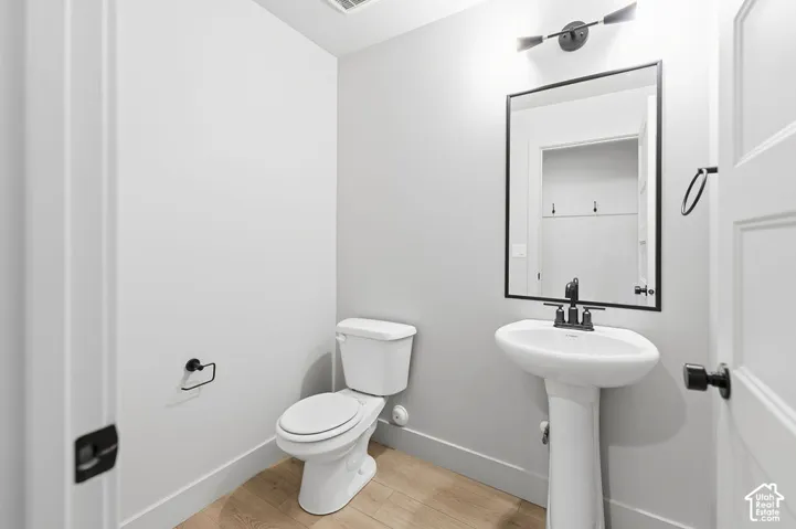 Pedestal sink with matte black faucet, framed mirror, two-light fixture, and wood-finish flooring
