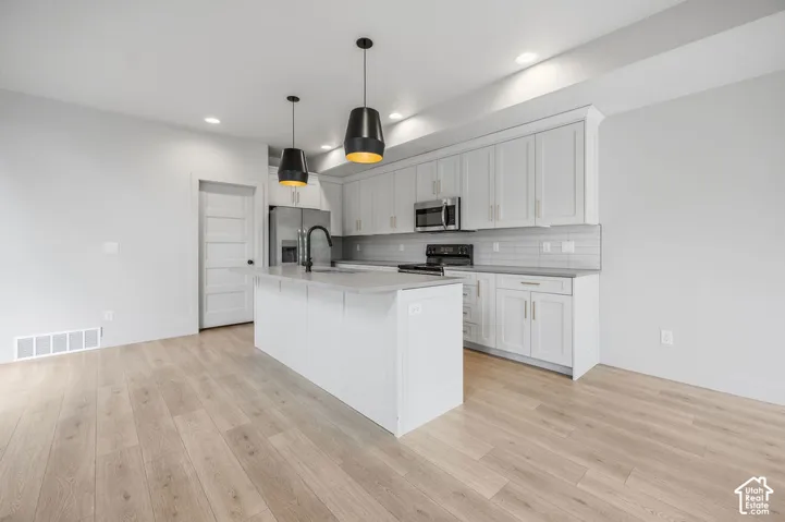 Kitchen featuring a central island with a quartz countertop, white cabinetry, wood-finish flooring, recessed lighting, and dual pendant fixtures