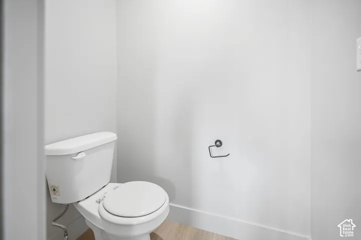 Neutral-toned restroom featuring a white porcelain toilet and a mounted matte black toilet paper holder over wood-finish flooring