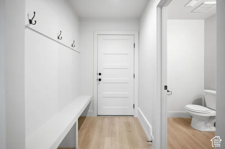 Entryway featuring wood-finish flooring, a built-in bench, wall-mounted matte black coat hooks, and a five-panel door with matching hardware