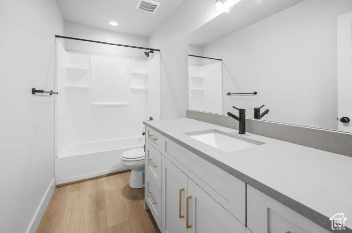 Bathroom featuring a vanity with quartz countertop, undermount sink, matte black faucet, shaker-style cabinetry, and wood-finish flooring