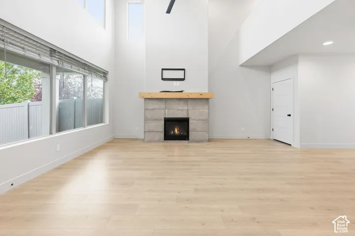 Expansive living area featuring vaulted ceilings, floor-to-ceiling windows, wood-finish flooring, and a stone-clad fireplace with a thick timber mantel