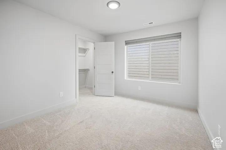 Neutral-toned wall-to-wall carpeting, five-panel interior door, walk-in closet with integrated shelving, and large dual-pane window