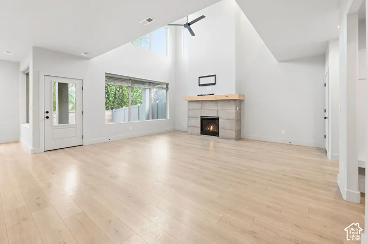 Vaulted ceilings featuring a fireplace with stone-style surround, wood-finish flooring, a wood mantel, and large windows