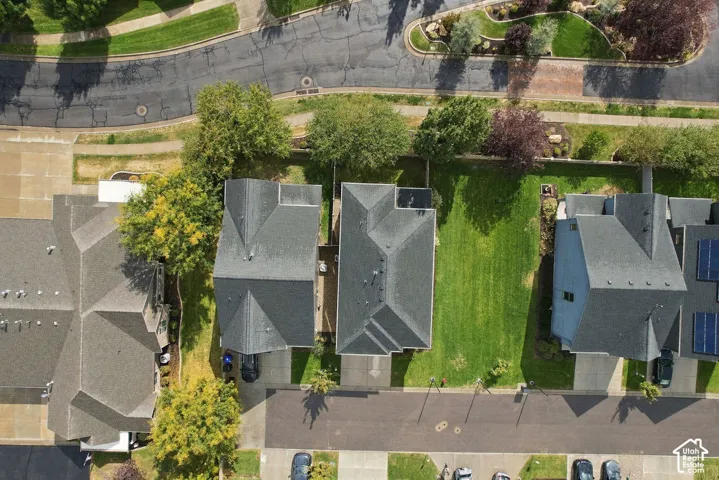Aerial perspective of a multi-level residential property featuring a dark-toned shingle roof, expansive side yard, paved driveway, and mature landscaping