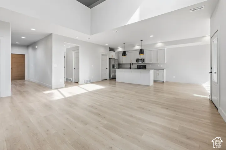 Open-concept interior featuring vaulted ceilings, wood-finish flooring, recessed lighting, and a kitchen island with pendant lighting and quartz countertops