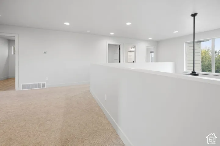 Neutral-toned interior space featuring recessed ceiling lighting, wall-to-wall carpeting, and a multi-pane window with a black pendant fixture