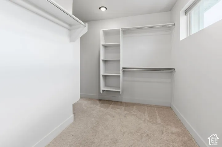 Walk-in closet featuring white built-in shelving, dual-tier hanging rods, neutral carpeting, and a recessed ceiling light