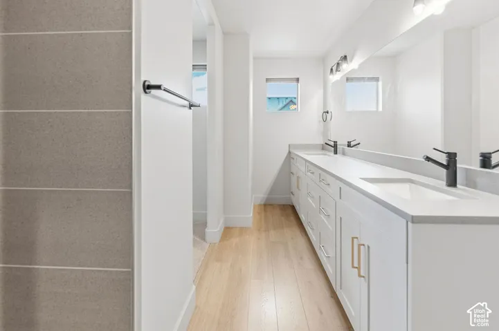 Dual-sink vanity with white cabinetry, light-toned countertop, and matte black hardware, paired with wood-finish flooring and full-width vanity mirror