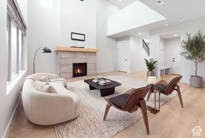 Living area featuring vaulted ceilings, wood-finish flooring, a fireplace with large-format tile surround, and a natural wood mantel