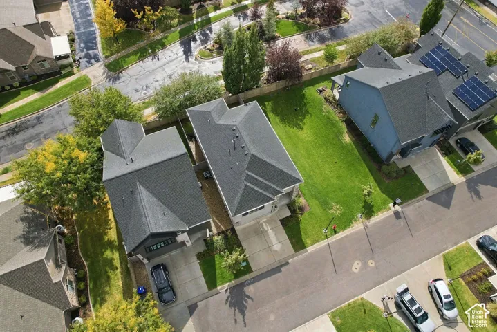 Aerial view of the residential property featuring a pitched shingle roof, concrete driveway, and expansive lawn area