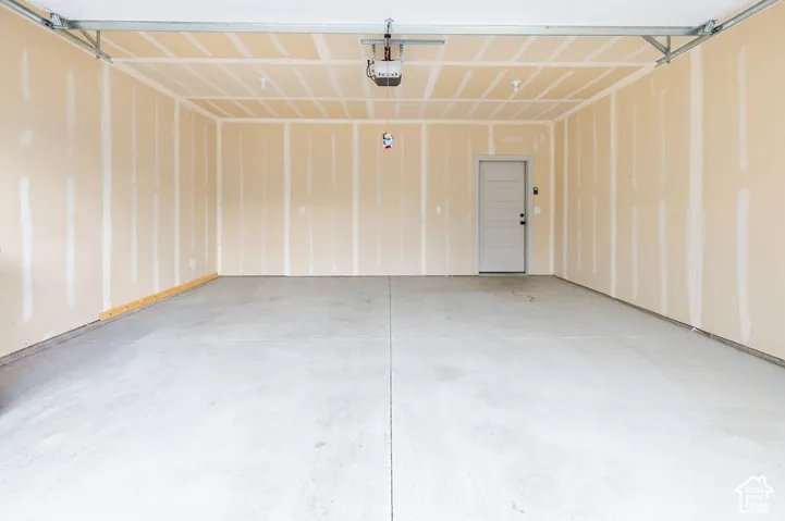 Finished garage featuring concrete flooring, drywall walls, a ceiling-mounted garage door opener, and a single-panel pedestrian door
