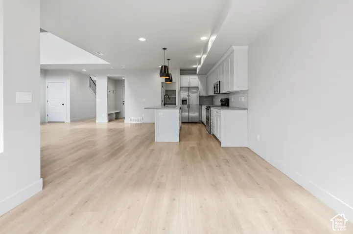 Open-concept kitchen featuring shaker-style cabinetry, an island with pendant lighting, stone-finish countertops, wood-finish flooring, and stainless steel appliances