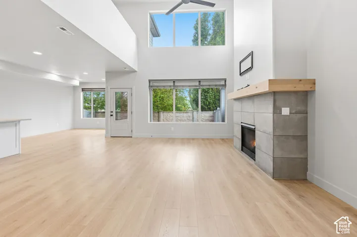 Double-height ceiling, wood-finish flooring, floor-to-ceiling fireplace with large-format concrete-style tile surround and natural wood mantel, and expansive multi-level windows