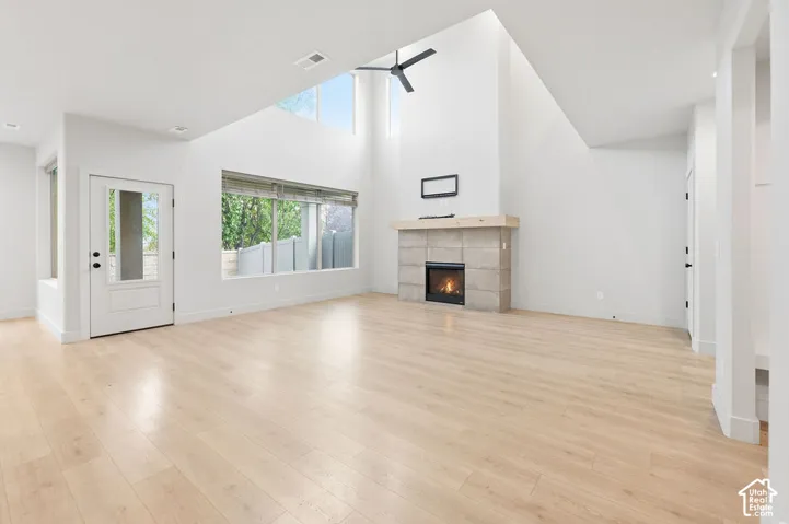 High-ceiling interior featuring wood-finish flooring, a full-height fireplace with stone-style surround, a light-toned wood mantel, and large windows