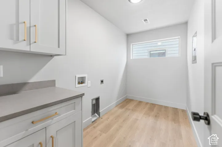 Utility space featuring light-toned wood-finish flooring, shaker-style cabinetry with gold-tone pulls, stone-composite countertops, and a horizontal window