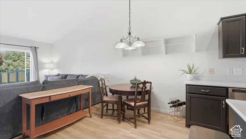 Vaulted ceilings, wood-finish flooring, dark cabinetry with light-toned countertops, and a three-light chandelier