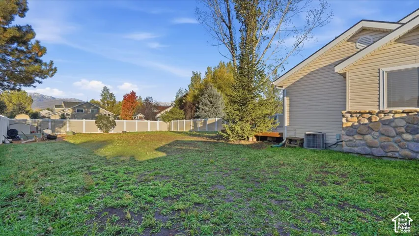 Backyard featuring a perimeter vinyl fence, natural stone veneer exterior siding, and mature coniferous trees