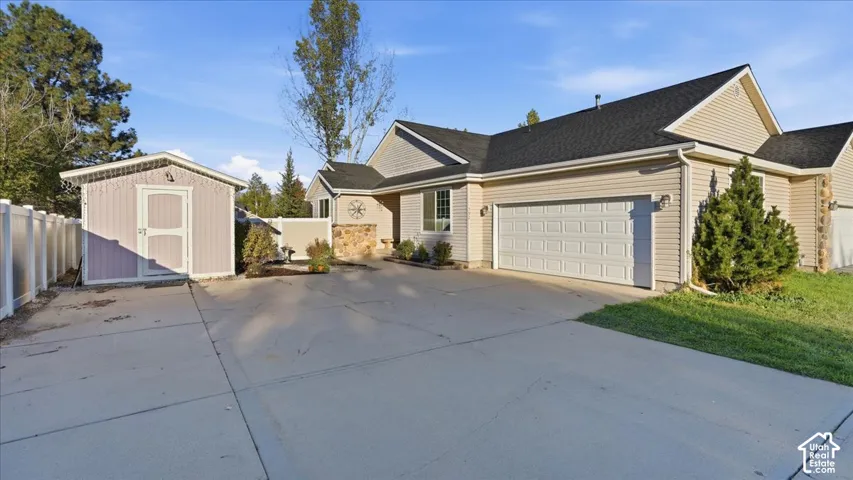 Single-level residence featuring horizontal vinyl siding, a two-car garage, stone masonry accents, a detached storage structure, and vinyl perimeter fencing