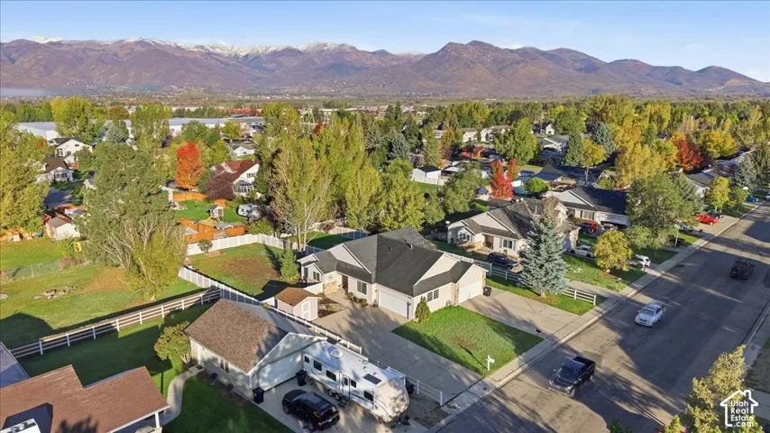Aerial perspective featuring a single-story residence with an attached multi-car garage, expansive fenced-in lot, and a detached structure, all set against a prominent mountain backdrop