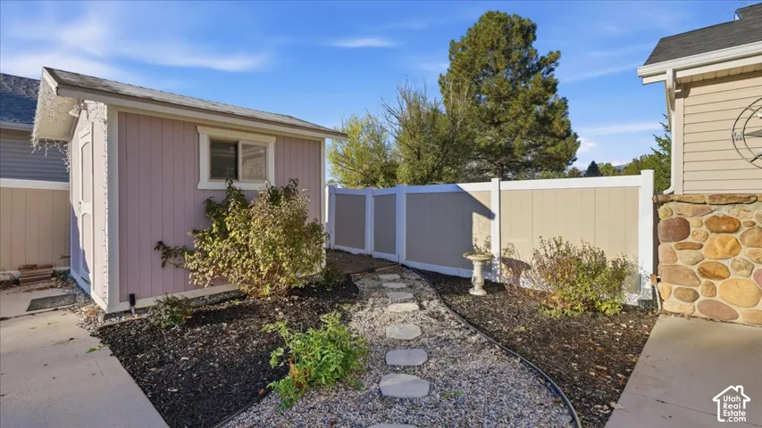 Detached storage structure featuring vertical siding, stone veneer accents on the primary exterior, a stone-paver walkway, and a full-height vinyl privacy fence