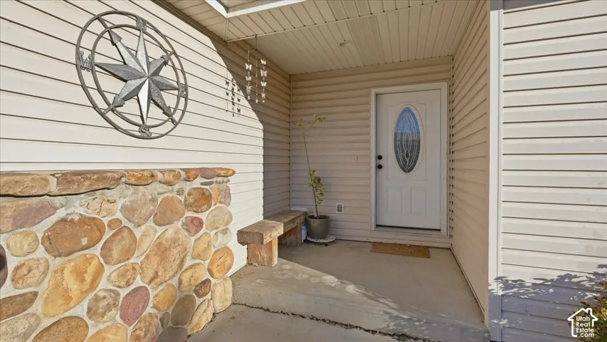 Covered entryway featuring horizontal vinyl siding, a natural stone veneer accent wall, and a central entry door with an oval glass insert