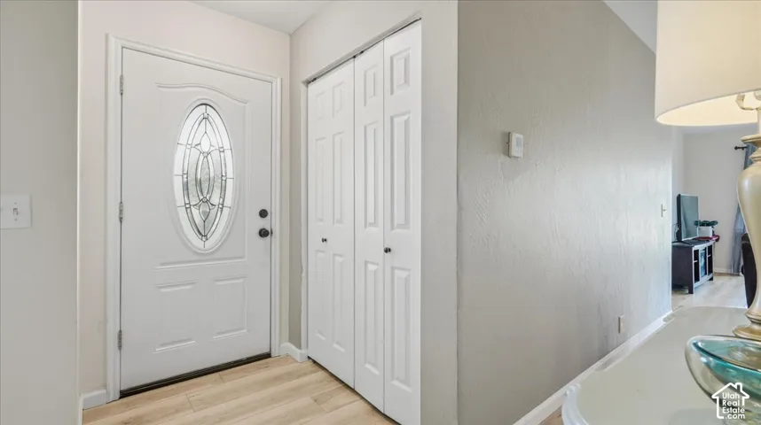Entryway featuring a white exterior door with an oval glass insert, wood-finish flooring, and a floor-to-ceiling bi-fold closet