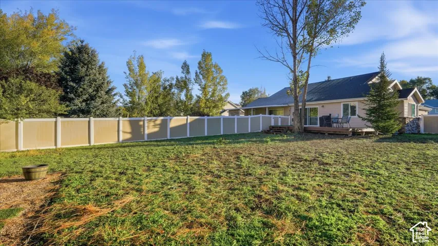 Expansive backyard featuring a full-perimeter privacy fence, mature trees, and a wooden deck