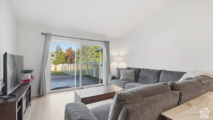 Living area featuring wood-finish flooring, vaulted ceilings, and a sliding glass door providing external access to a paved patio and fenced yard