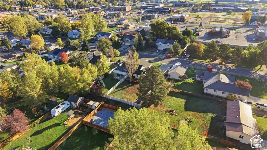 Aerial perspective of a residential lot featuring a fenced backyard, mature trees, and a ground-level concrete patio