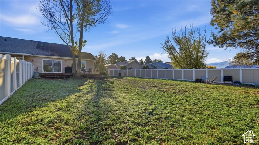 Backyard featuring an expansive lawn, full-perimeter vinyl fencing, and a raised wooden deck